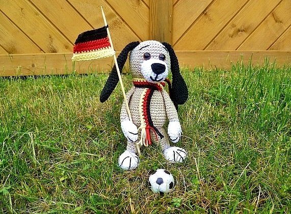 Gehäkelter Amigurumi-Hund mit Deutschlandflagge und Fußball auf Wiese
