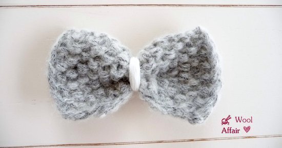 Gestrickte Schleife in Grau-Melange mit weißer Wicklung in der Mitte auf hellem Hintergrund