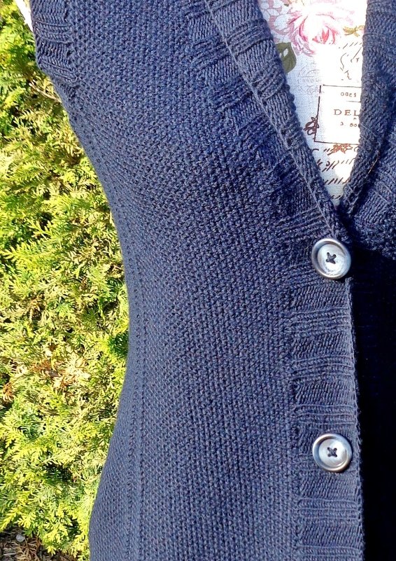 Close-up of navy seed-stitch sleeveless cardigan on a dress form showing V-neck, ribbed button band, and two buttons