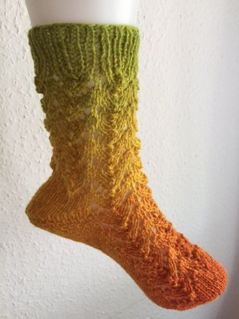 Gestrickte Damensocke in Olivgrün, Gelb und Orange mit Ajourmuster auf weißem Fußmodell.