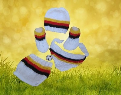 Weißes Baby-Strickset mit Streifen in Schwarz, Rot und Gold/Gelb: Mütze, Schühchen, Dreieckstuch, Windelhose und kleiner Fußball.