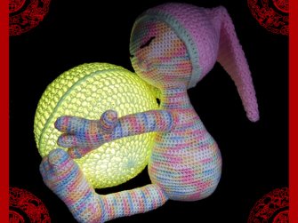 Gehäkeltes Amigurumi-Häschen in Pastellfarben hält eine leuchtende Kugel