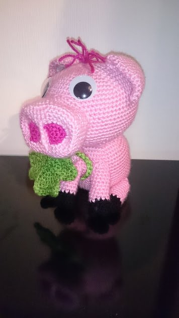 Gehäkeltes rosa Schwein hält grünes Kleeblatt