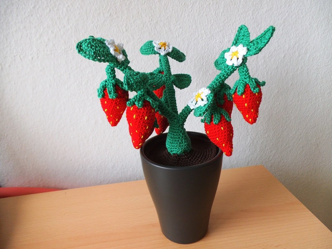 Gehäkelte Erdbeerpflanze mit roten Erdbeeren, weißen Blüten und dunklem Topf