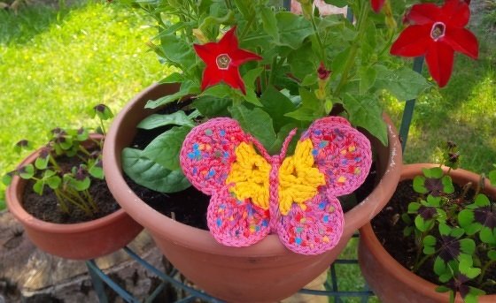 Gehäkelte Schmetterlings-Applikation in Pink und Gelb auf einem Tontopf