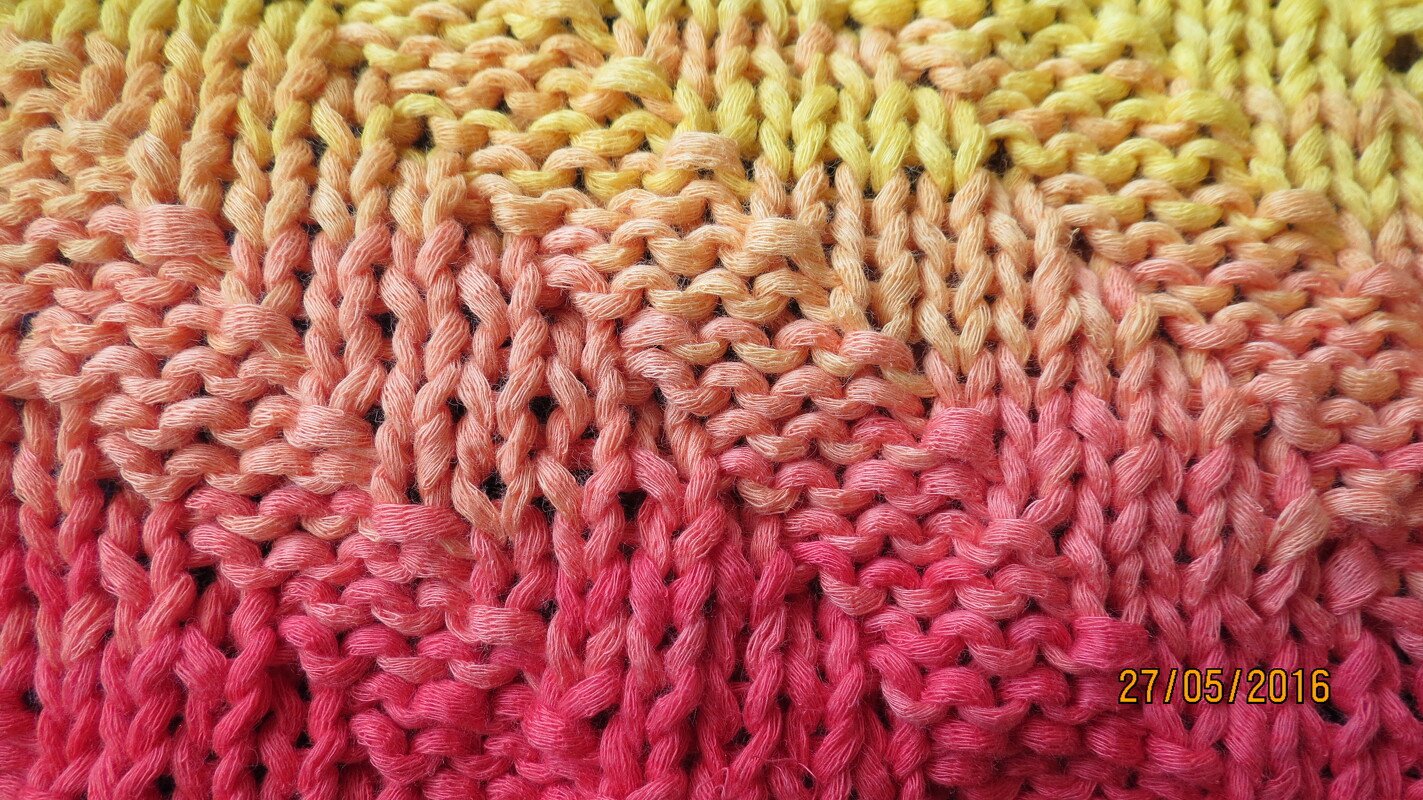 Nahaufnahme gestrickter Maschen mit Farbverlauf Gelb–Orange–Pink.