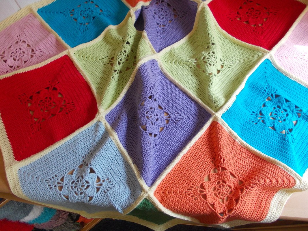Nahaufnahme einer bunten Häkeldecke aus quadratischen Feldern mit Blumenmotiven