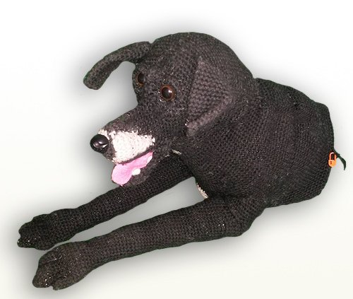 Gehäkelter schwarzer Amigurumi-Hund, liegend, mit weißer Schnauze und herausgestreckter Zunge