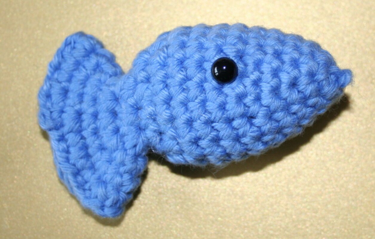 Blauer gehäkelter Amigurumi-Fisch mit schwarzem Knopfauge auf hellem Hintergrund.