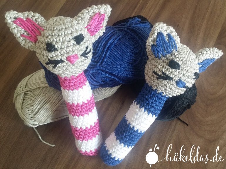 Zwei gehäkelte Babyrasseln mit Katzenköpfen und gestreiften Griffen