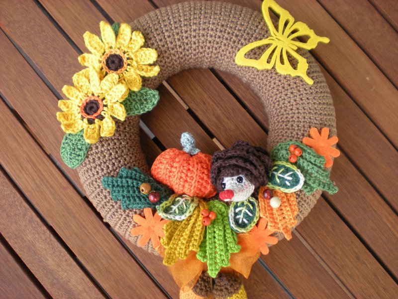 Brown crocheted wreath with yellow sunflowers, orange pumpkin, a small crocheted figure, green leaves and a yellow butterfly