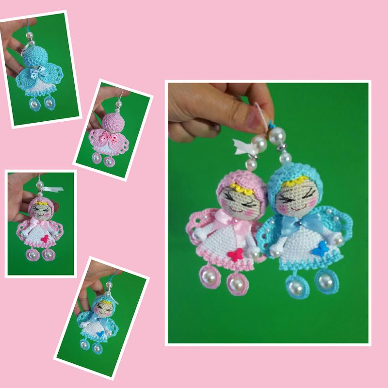 Zwei gehäkelte Amigurumi-Engelchen, eines rosa mit Herz, eines hellblau mit Schmetterling, beide mit Perlen als Beine und Aufhängung, an einer Hand gehalten vor grünem Hintergrund.