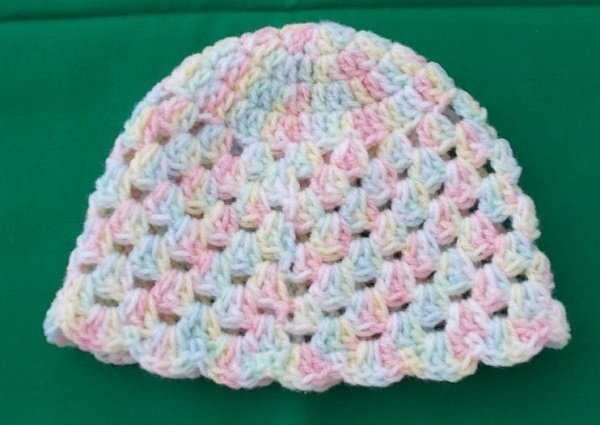 Gehäkelte Babymütze aus pastellfarbenem, mehrfarbigem Garn auf grünem Hintergrund