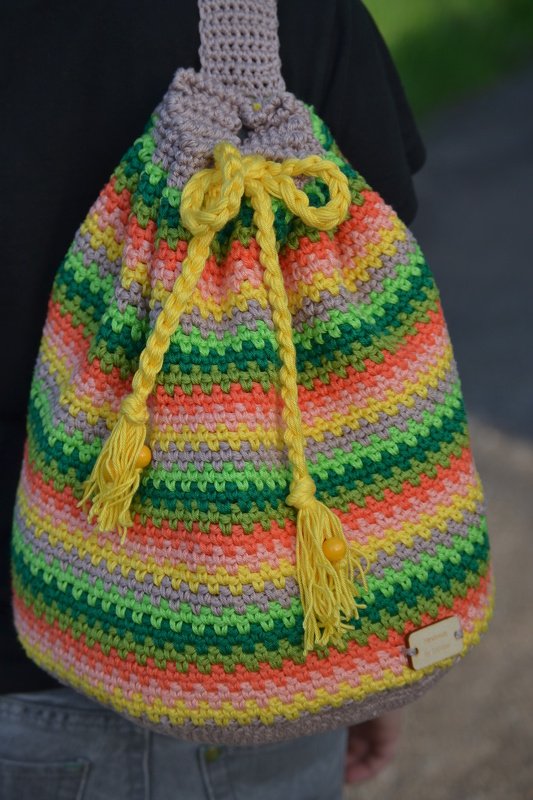 Bunter gehäkelter Rucksack mit farbigen Streifen, gelbem Kordelzug, Quasten und Perlen.