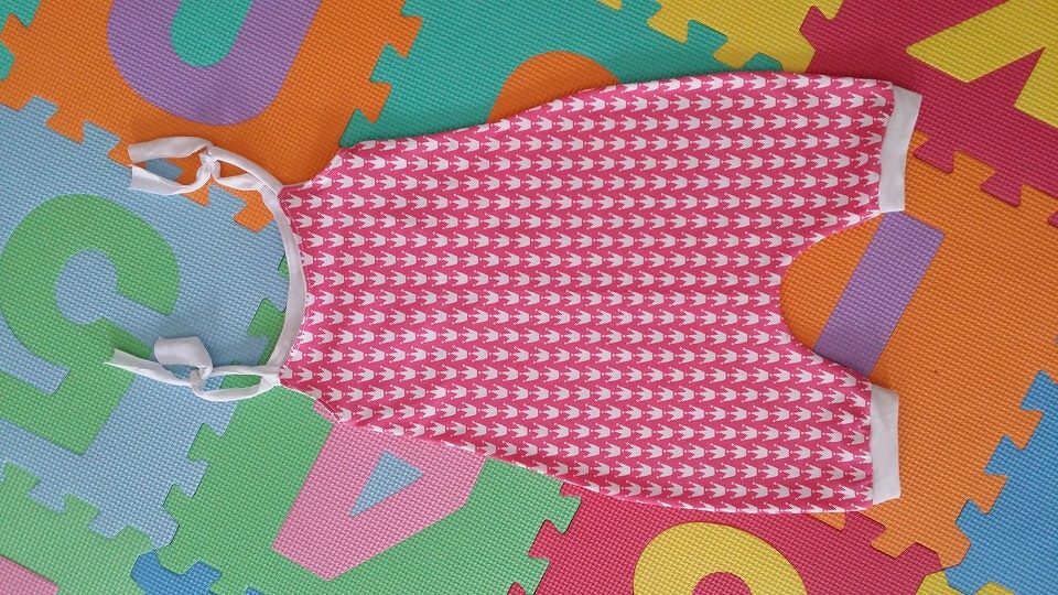 Detailaufnahme: rosa Babystrampler mit weißen Kronen auf bunter Spielmatte
