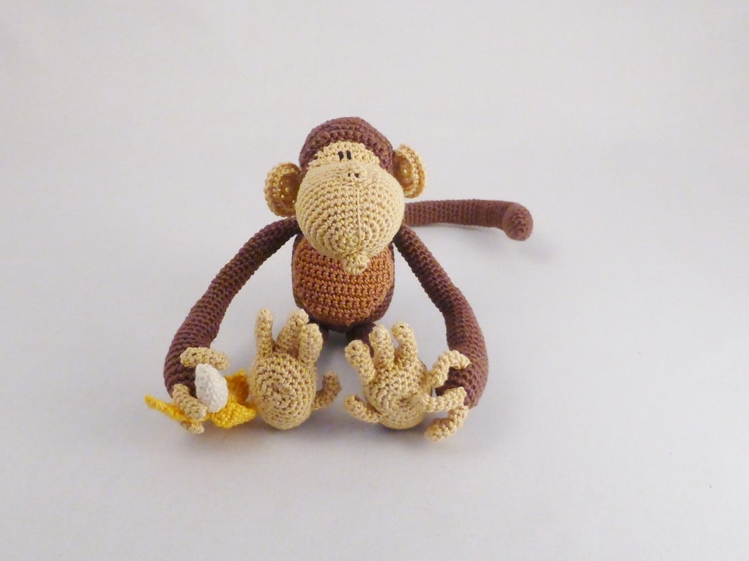 gehäkelter Amigurumi-Affe in Braun und Beige, sitzt mit Banane