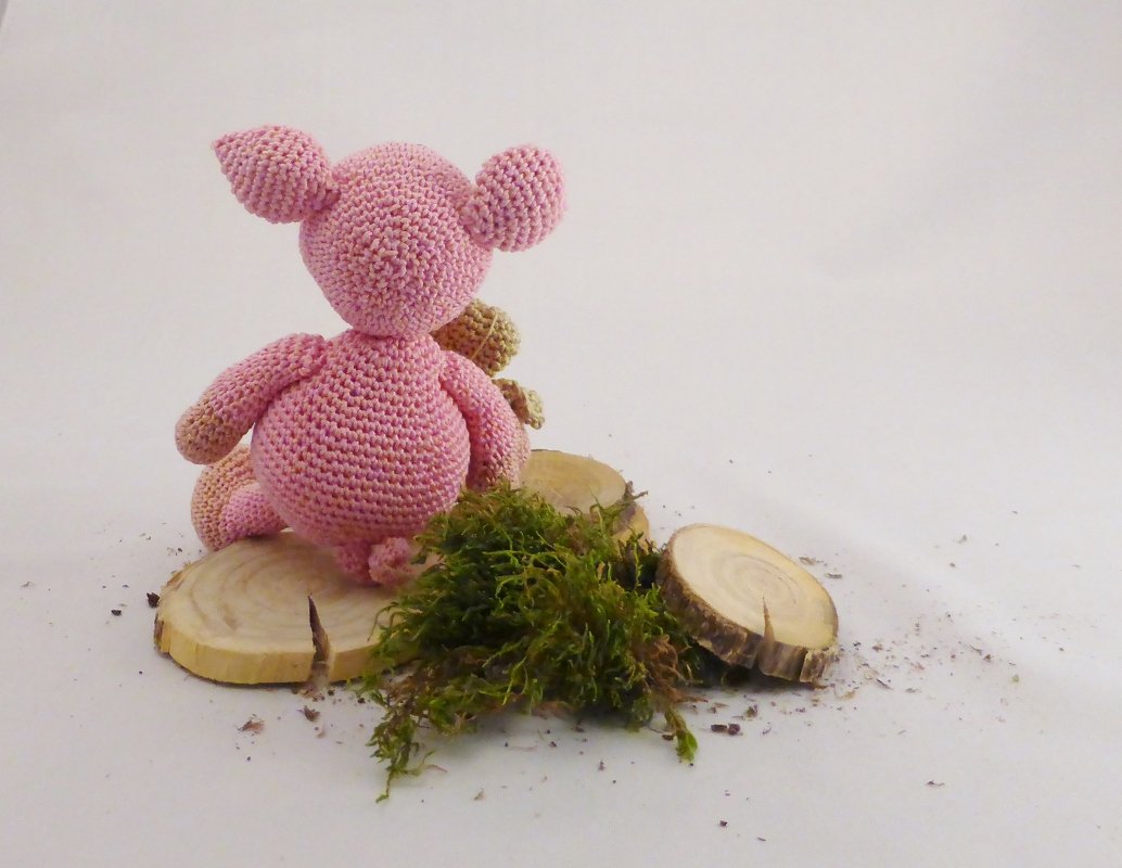 Rückansicht eines rosa gehäkelten Amigurumi-Schweins auf Holzscheiben mit Moos