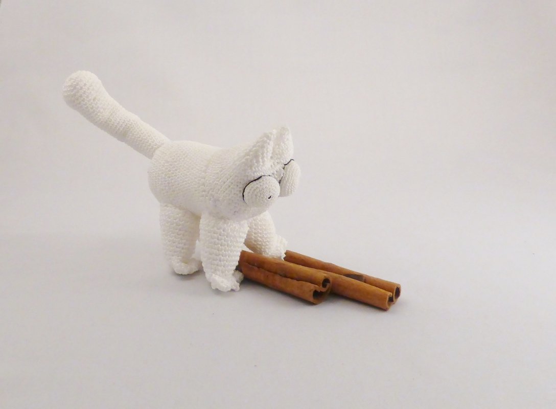 Weißer gehäkelter Katzen-Amigurumi mit drei Zimtstangen auf hellem Untergrund
