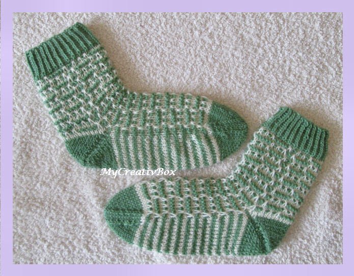 Paar gestrickter Kindersocken in Grün und Weiß mit Rippenbündchen und gestreiftem Fuß