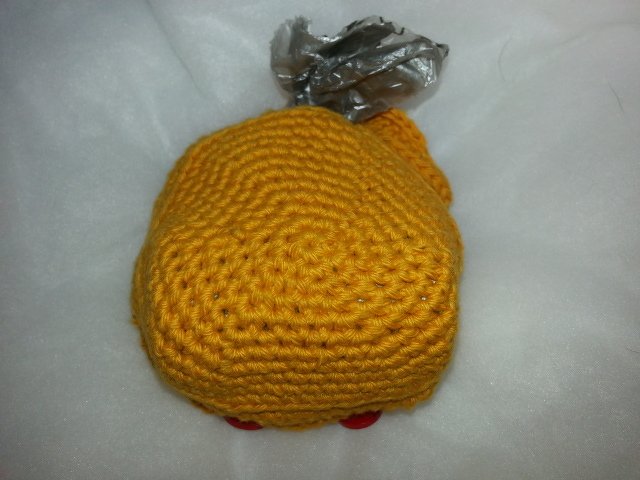 Gelbes gehäkeltes Hähnchen-Spielzeug mit silbernem Foliendetail auf hellem Hintergrund