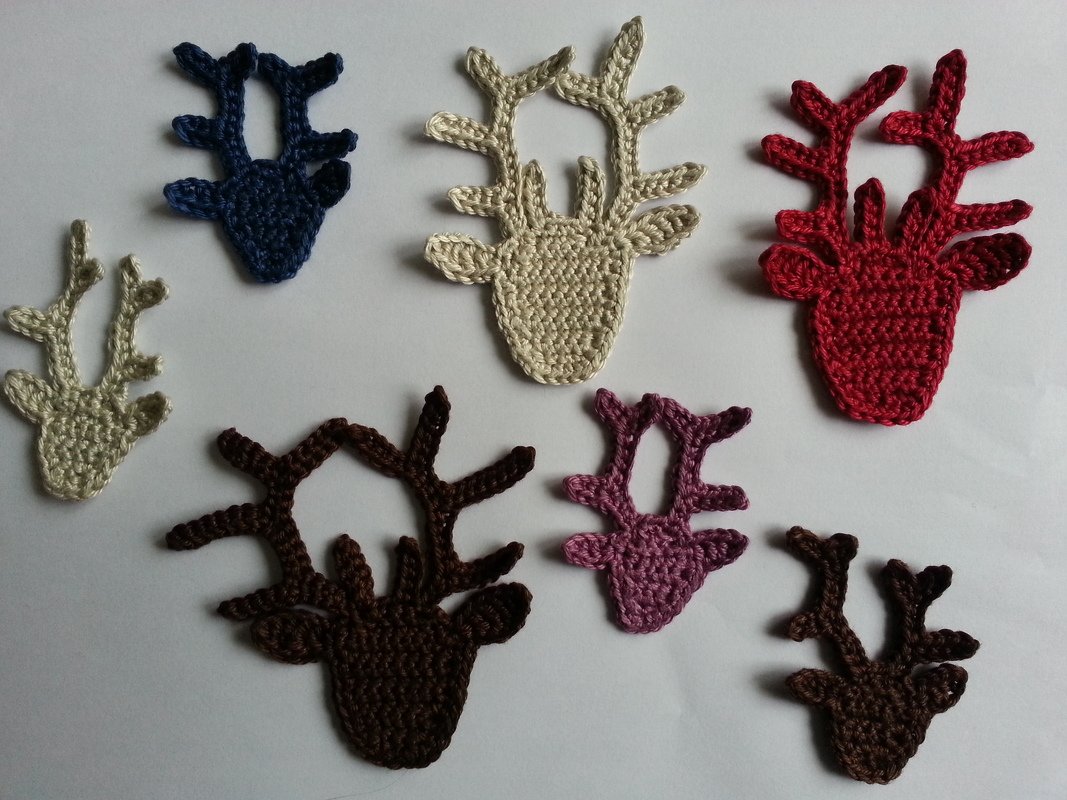 Verschiedene Größen und Farben gehäkelter Hirschkopf-Applikationen auf weißer Fläche