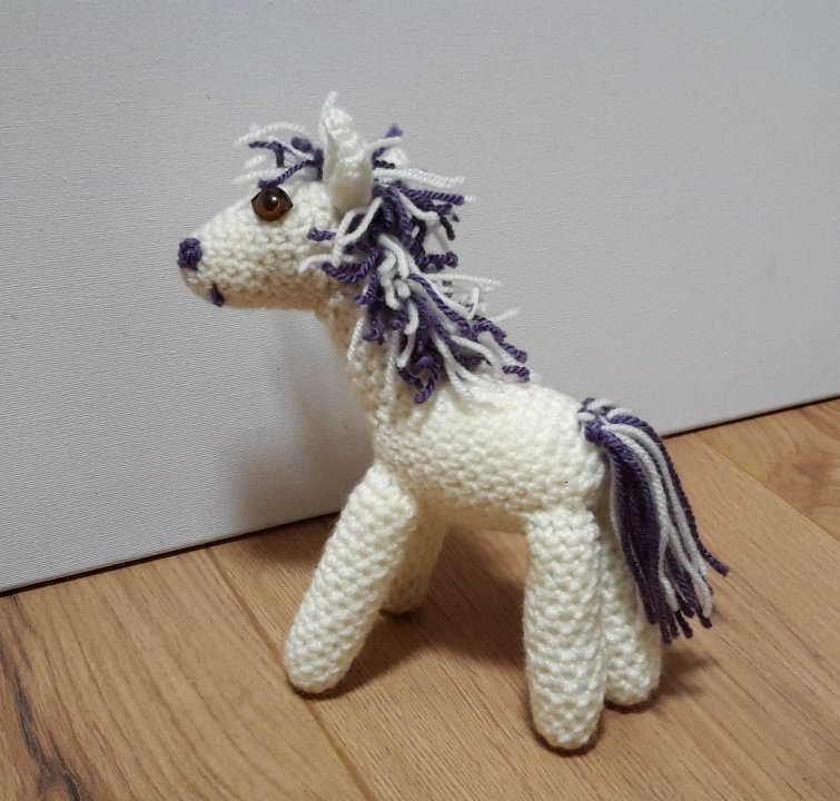 Weißes gehäkeltes Einhorn mit lila-weißer Mähne und Schweif