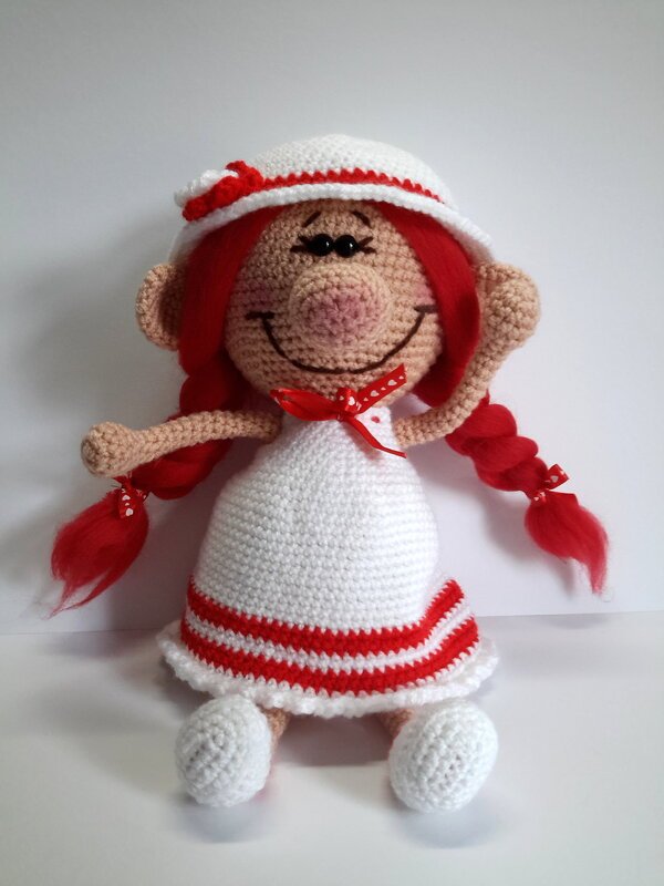 Gehäkelte Amigurumi-Puppe mit roten Zöpfen, weißem Kleid und Hut, lächelnd