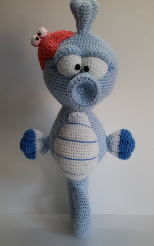 Hellblaues gehäkeltes Seepferdchen-Amigurumi mit weiß gestreiftem Bauch und roter Mütze