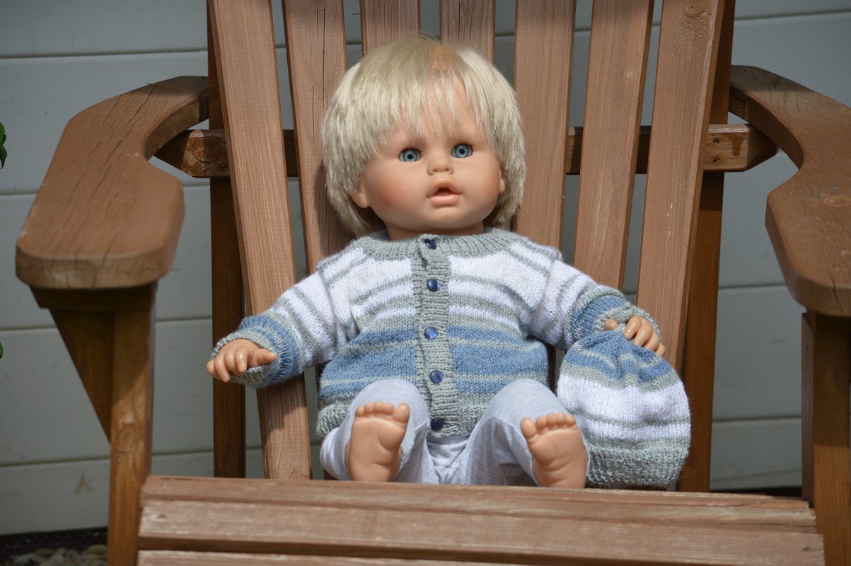 Zweiteiliges gestricktes Babyset mit Knopfjacke und passender Mütze in Blau, Weiß und Grau auf einem Holzstuhl