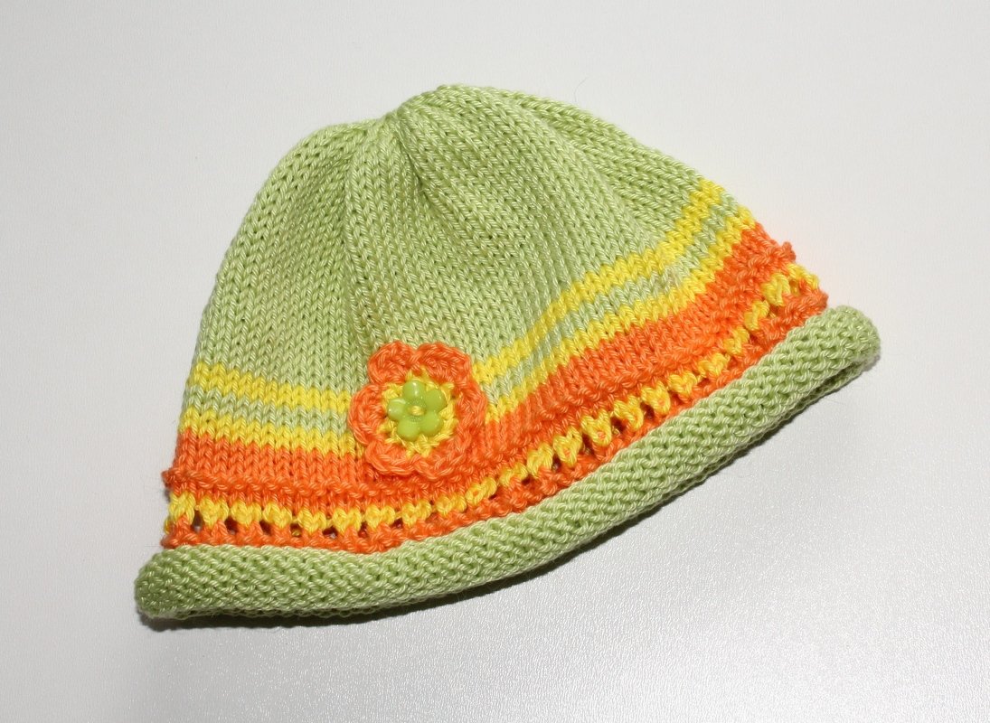 Hellgrüne gestrickte Babymütze mit orange-gelben Streifen und kleiner Blüte