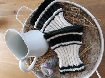 Nahaufnahme gestrickter weißer Herren-Armstulpen mit Rippenmuster und dunkelgrünen Kontraststreifen in einer Dekoschale