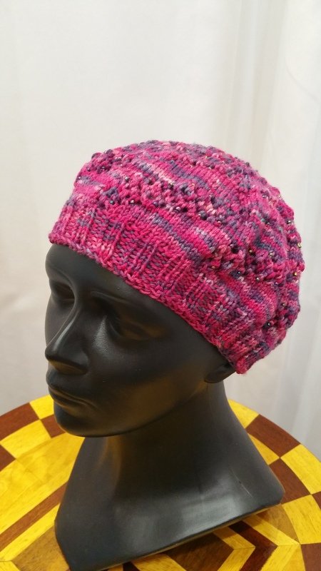 Pink gestrickte Damenmütze mit Noppenmuster und eingearbeiteten Perlen auf schwarzem Schaufensterkopf