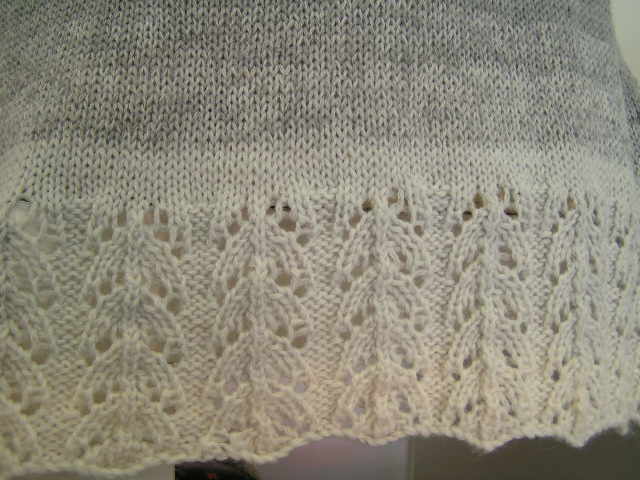 Detail: gestrickter Stoff mit hellgrauem zu weißem Farbverlauf und Blatt-Lochbordüre am Saum