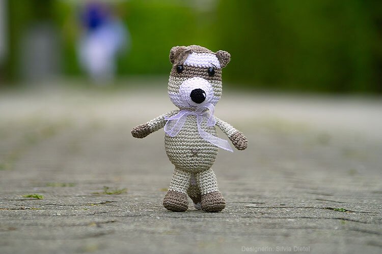 Gehäkeltes Amigurumi-Tier in Beige und Braun mit dunkler Maske und Schleife am Hals