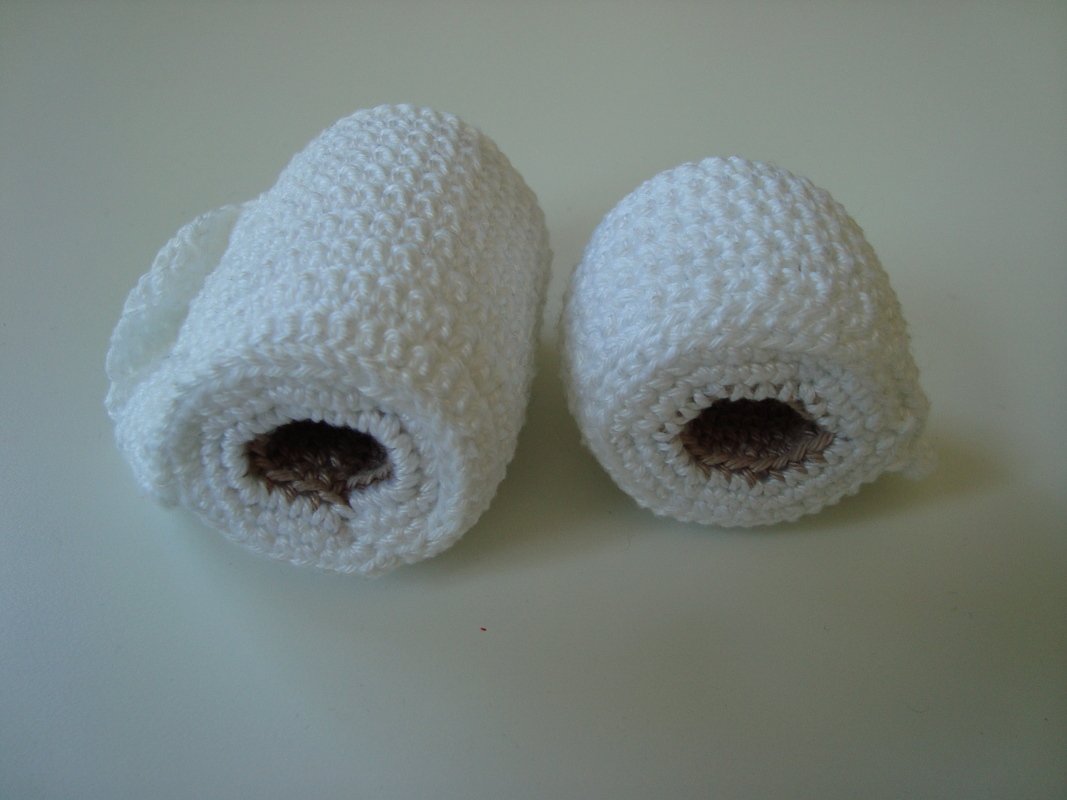 Zwei gehäkelte weiße Rollen mit braunem Innenkern auf hellem Untergrund