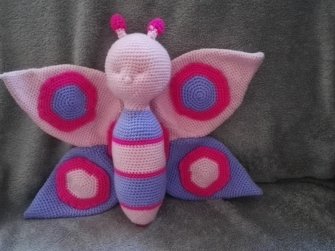 Gehäkelter Amigurumi‑Schmetterling in Rosa und Lila liegend