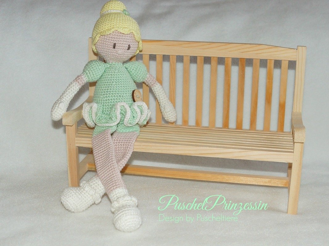 Gehäkelte Amigurumi-Ballerina in Hellgrün und Rosa auf Mini-Holzbank