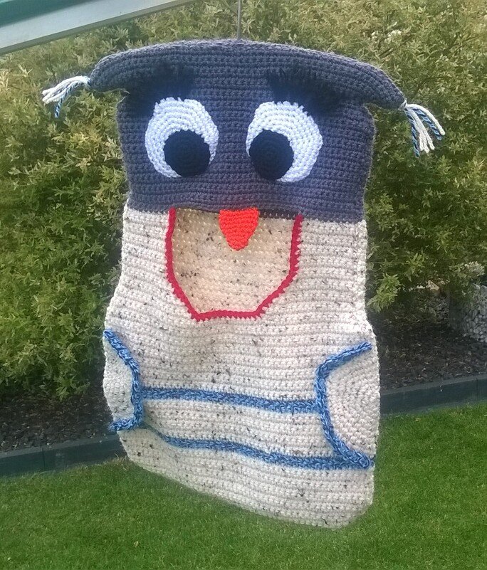 Gehäkeltes Eulen-Utensilo in Grau-Beige mit großen Augen und orangefarbenem Schnabel, hängend im Garten