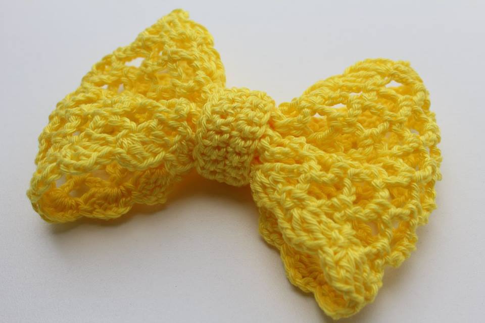 Gelbe Häkelschleife mit offenem Muster auf weißem Hintergrund