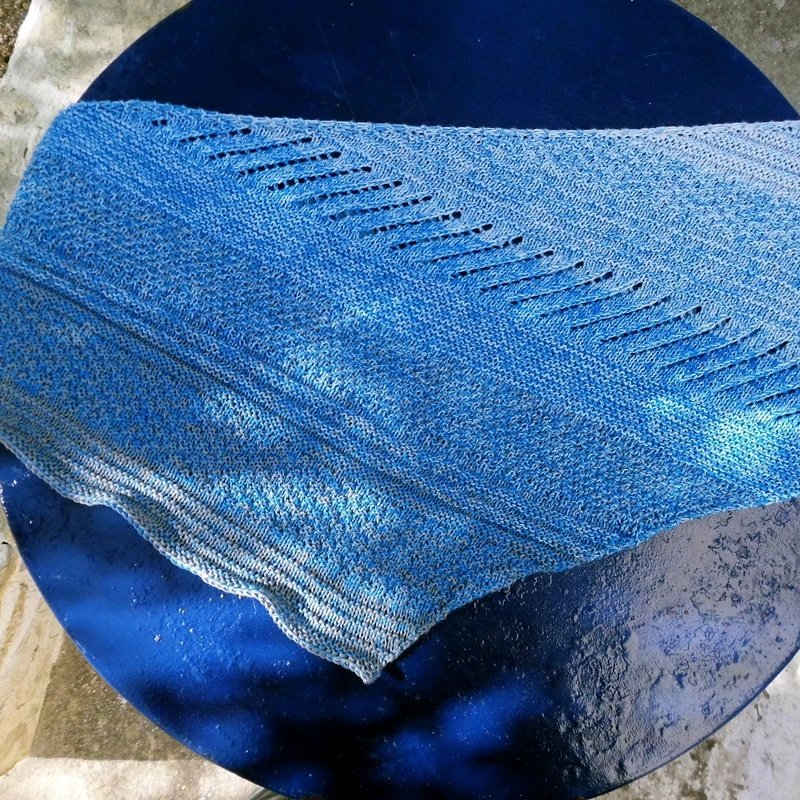 Gestricktes blaues Dreieckstuch mit diagonalen Lochreihen auf dunklem runden Untergrund