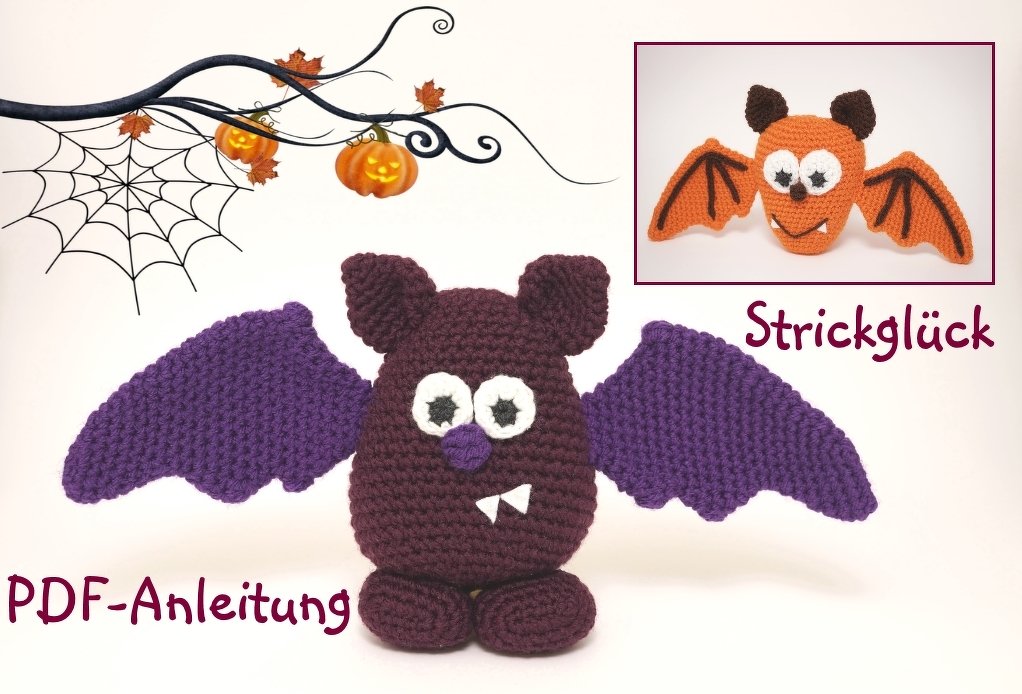 Gehäkelte Fledermaus in dunkelrot mit lila Flügeln und sichtbaren Zähnen vor Halloween-Dekor