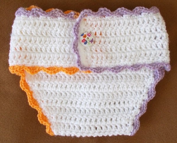 Gehäkelte weiße Windelhose mit lila- und orangefarbenem Wellenrand und Blumenknopf