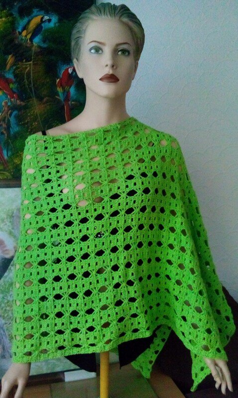 Grüner Damen-Poncho mit offenem Häkelmuster auf Puppe drapiert