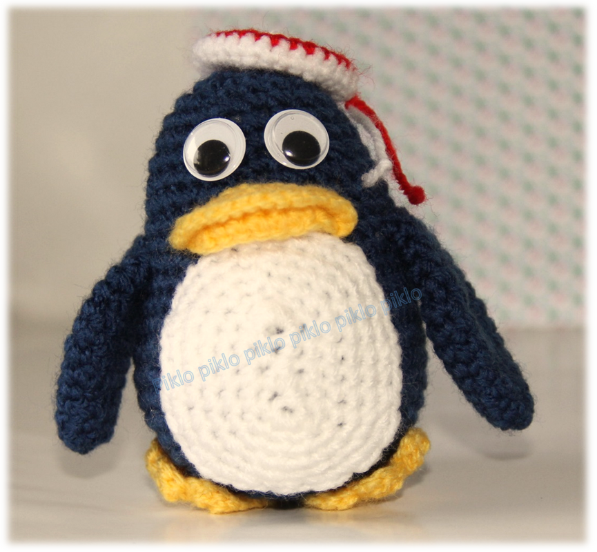 Gehäkelter Pinguin-Amigurumi in Dunkelblau mit weißem Bauch, gelbem Schnabel und rot-weiß gestreifter Matrosenmütze