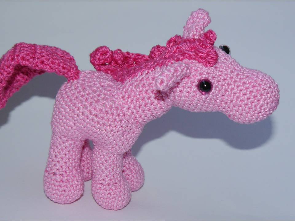 Seitenansicht eines rosa gehäkelten Einhorn-Amigurumi mit dunkler Mähne und glänzenden Augen