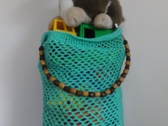 Türkisfarbene gehäkelte Netztasche mit Holzperlenhenkel, gefüllt mit Kinderspielzeug und Bausteinen
