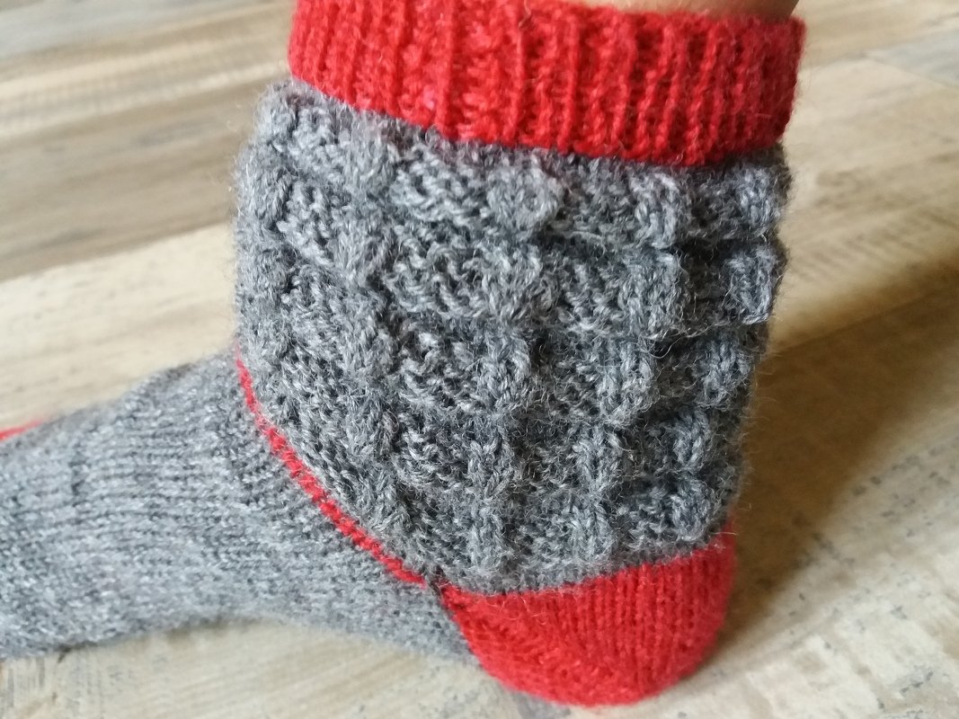 Grau gestrickte Socke mit Zopfmuster, rotem Bündchen und roter Ferse, Seitenansicht