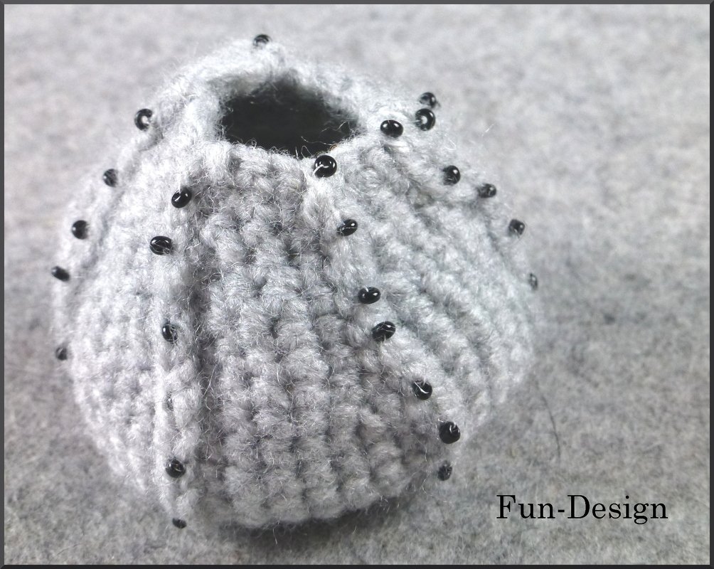Gehäkelter runder Seeigel aus grauem Garn mit kleinen schwarzen Perlen