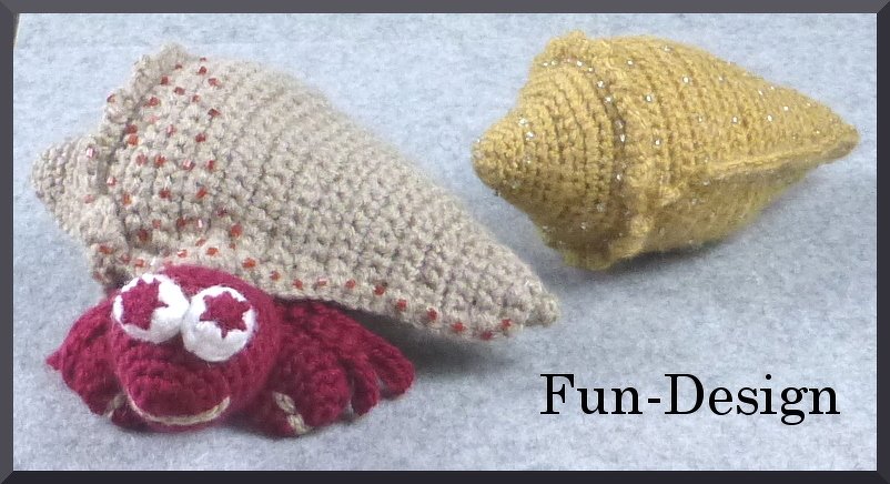 Rote gehäkelte Amigurumi-Krabbe neben einer beigen Muschel mit Perlen und einer gelben Muschel mit Glitzer auf hellem Untergrund.