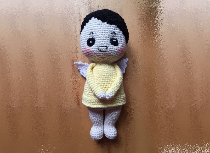 Gehäkelte Amigurumi-Engelpuppe in gelbem Kleid mit schwarzen Haaren und weißen Flügeln